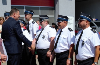 Mężczyzna podający dłoń strażakowi, Dookoła stoi kilkunastu druhów, 