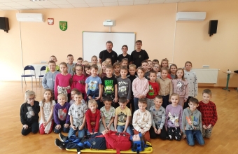 Strażacy wraz z dużą grupą dzieci w szkolnej sali 